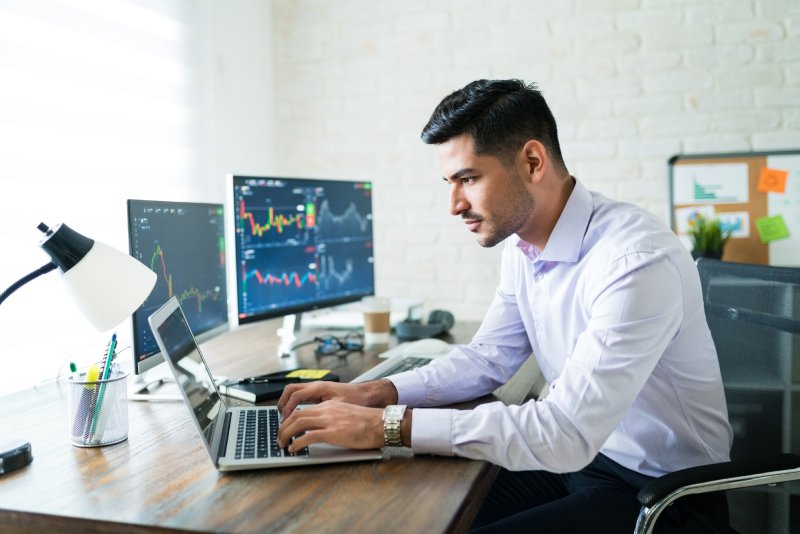 Man trading on his laptop and two monitors